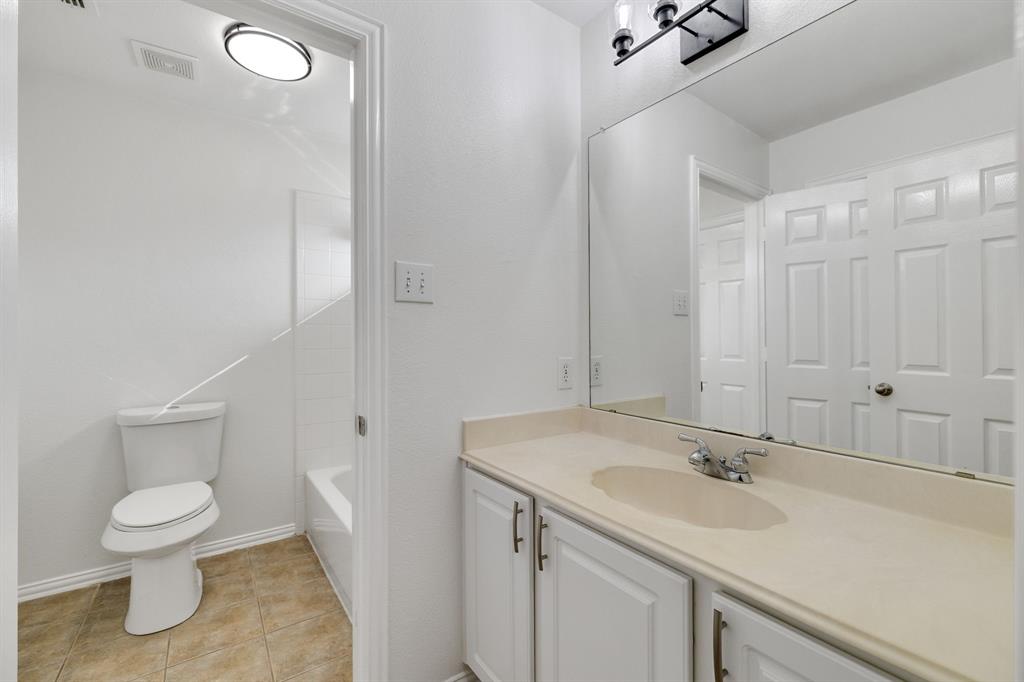 White vanity with cabinet storage, integrated sink, large wall-mounted mirror, and tile flooring