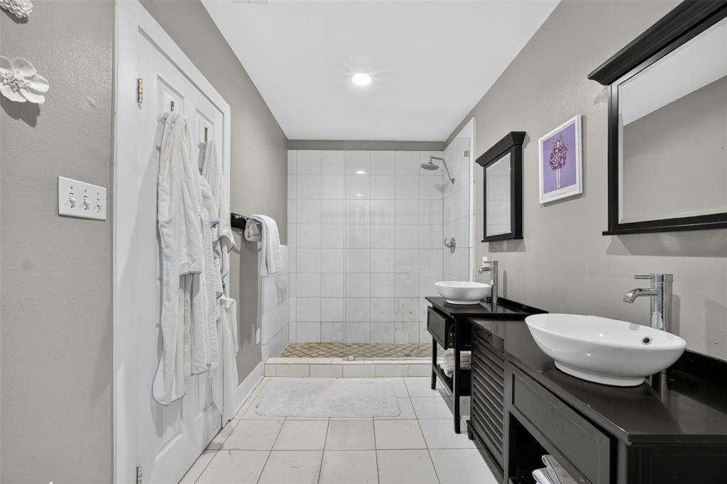 Spa-inspired primary bathroom featuring a walk-in shower with subway tile surround, dual vanities with vessel sinks and matte black hardware, recessed ceiling lighting, and neutral tile flooring throughout