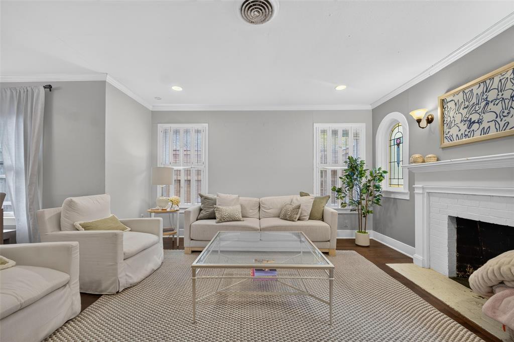 Recessed lighting with crown molding, wood-finish flooring, and a fireplace with a white mantel and hearth