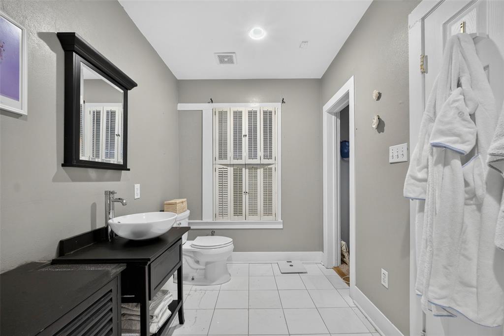 White vessel sink with chrome faucet, black vanity with open shelving, recessed lighting, and white tile flooring