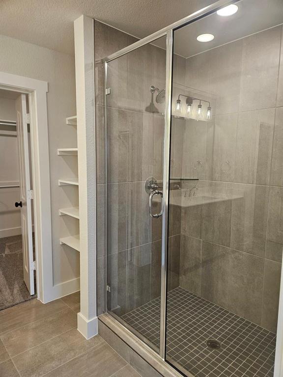 Frameless glass shower enclosure with a rainfall showerhead, recessed lighting, and wall-mounted shelving