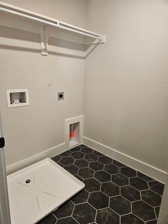 White shelf and hanging rod, textured white walls, utility hookups, and hexagonal floor tiling