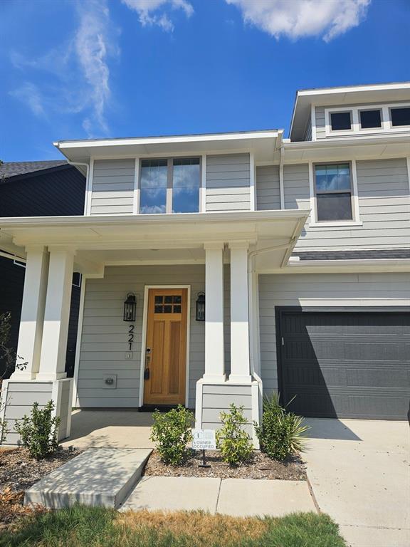 Light gray horizontal siding, prominent white columns, wood-finish entry door, dark garage door, and upper-level windows