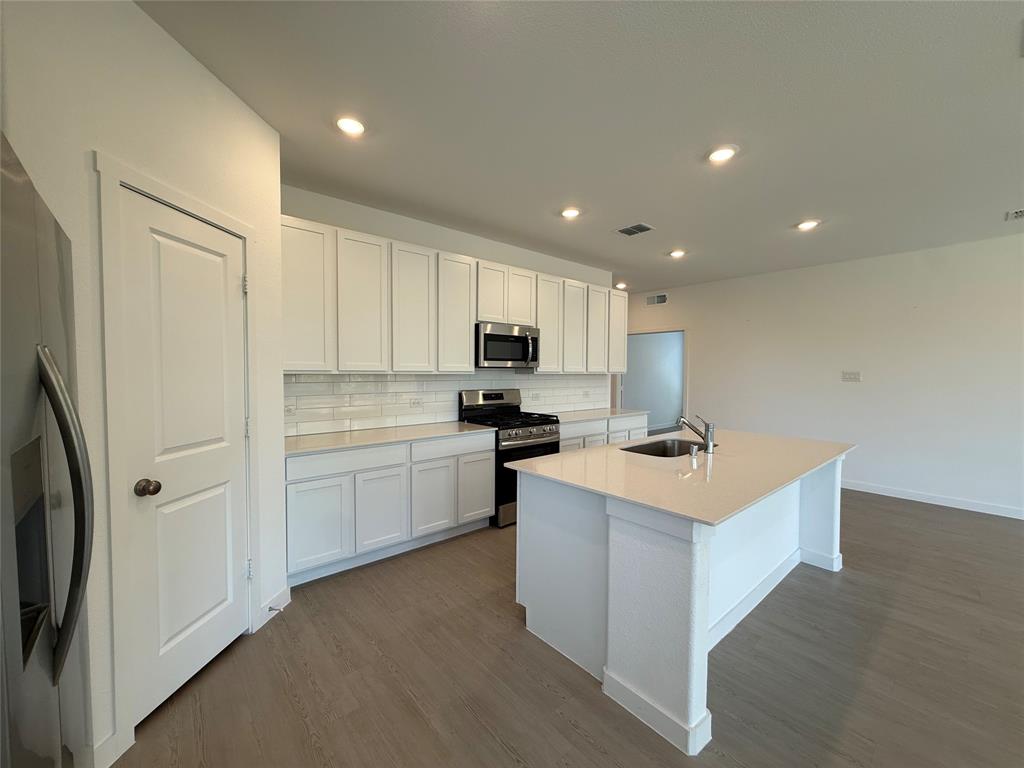 Open-concept kitchen featuring white cabinetry, stainless steel appliances, a center island with an integrated sink, recessed lighting, and wood-finish flooring
