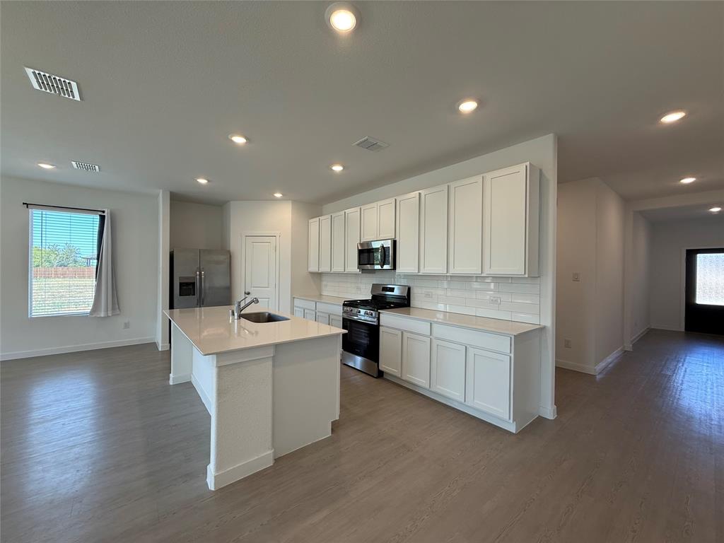 Kitchen featuring a central island with sink, stainless steel appliances, white cabinetry, and subway tile backsplash