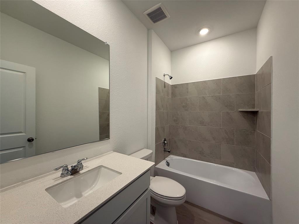 Bathroom featuring a vanity with an integrated sink, polished chrome fixtures, a full-width mirror, and a tiled tub surround with an integrated shelf