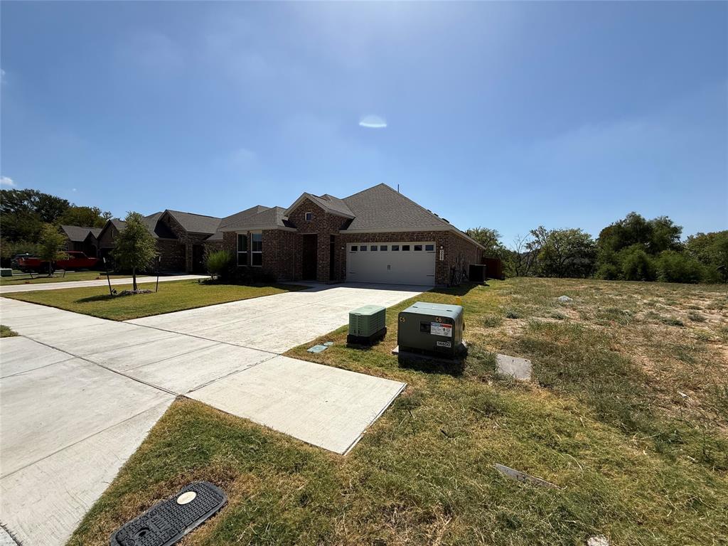 Brick exterior, attached garage, concrete driveway, front yard landscaping, natural terrain