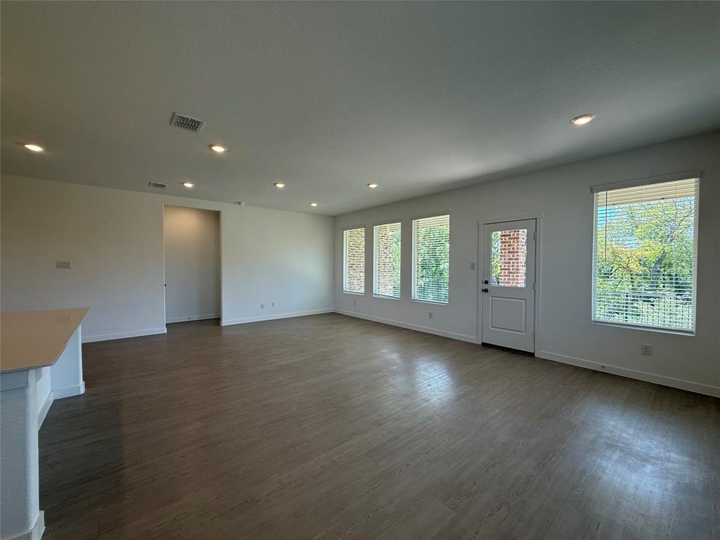 Open-concept living space with wood-finish flooring, recessed lighting, multiple windows with blinds, and a white paneled door with an integrated window