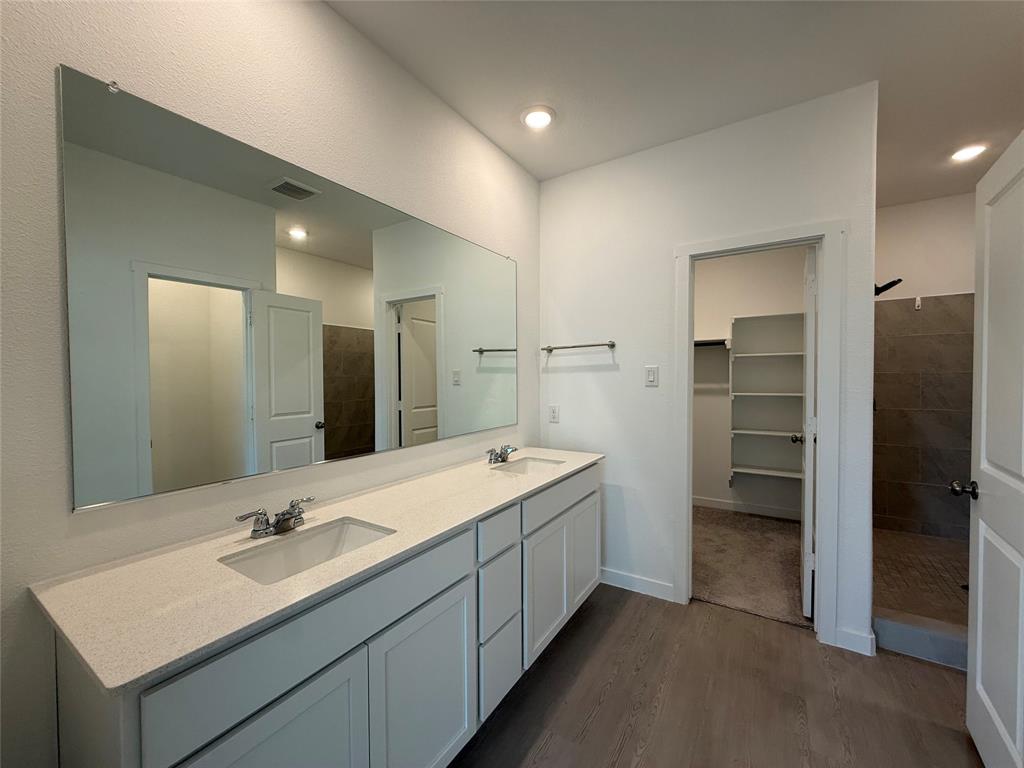 Dual vanity with light-toned countertop and integrated sinks, wood-finish flooring, and built-in shelving in an adjacent space