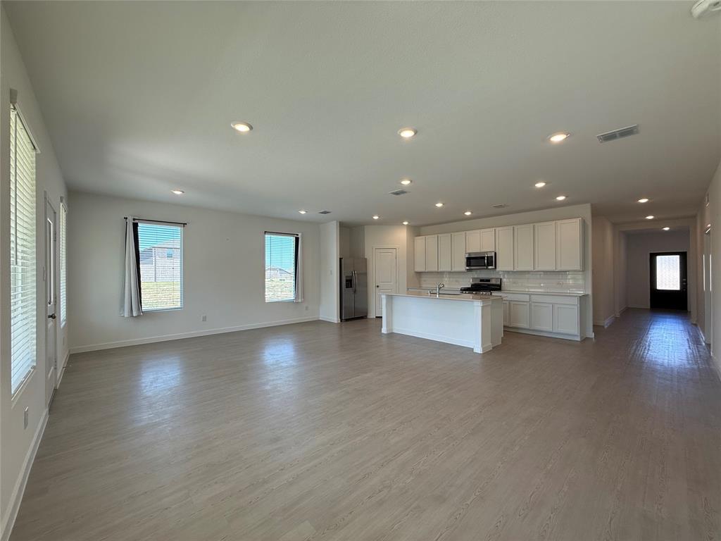 Open-concept living space featuring wood-finish flooring, recessed lighting, and a kitchen with white cabinetry, a center island, and stainless steel appliances