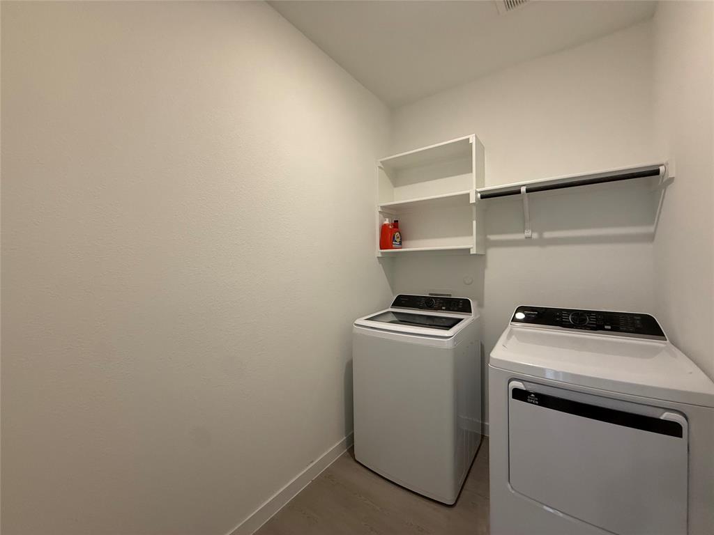 Dedicated laundry area featuring built-in white shelving, a clothing rod, and wood-finish flooring