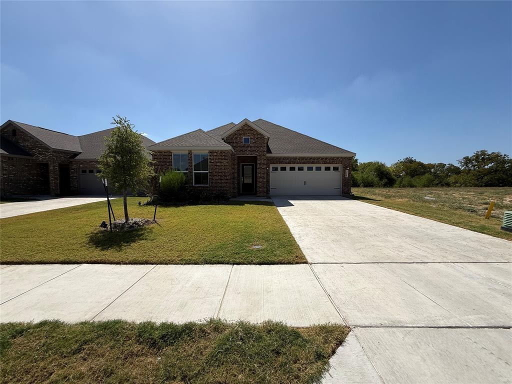 Brick exterior with an attached garage, paved driveway, and established front yard landscaping