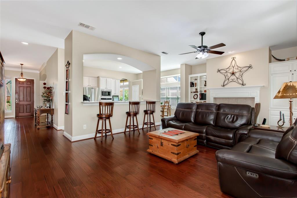 Hardwood-finish flooring throughout, fireplace with mantle, built-in shelving, ceiling fan, and arched pass-through to the kitchen