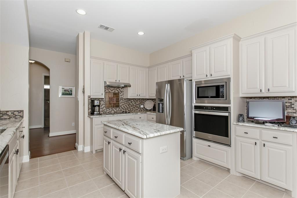 Kitchen featuring a center island with light-toned countertop, white cabinetry with dark hardware, recessed lighting, and stainless steel appliances including a built-in oven and microwave