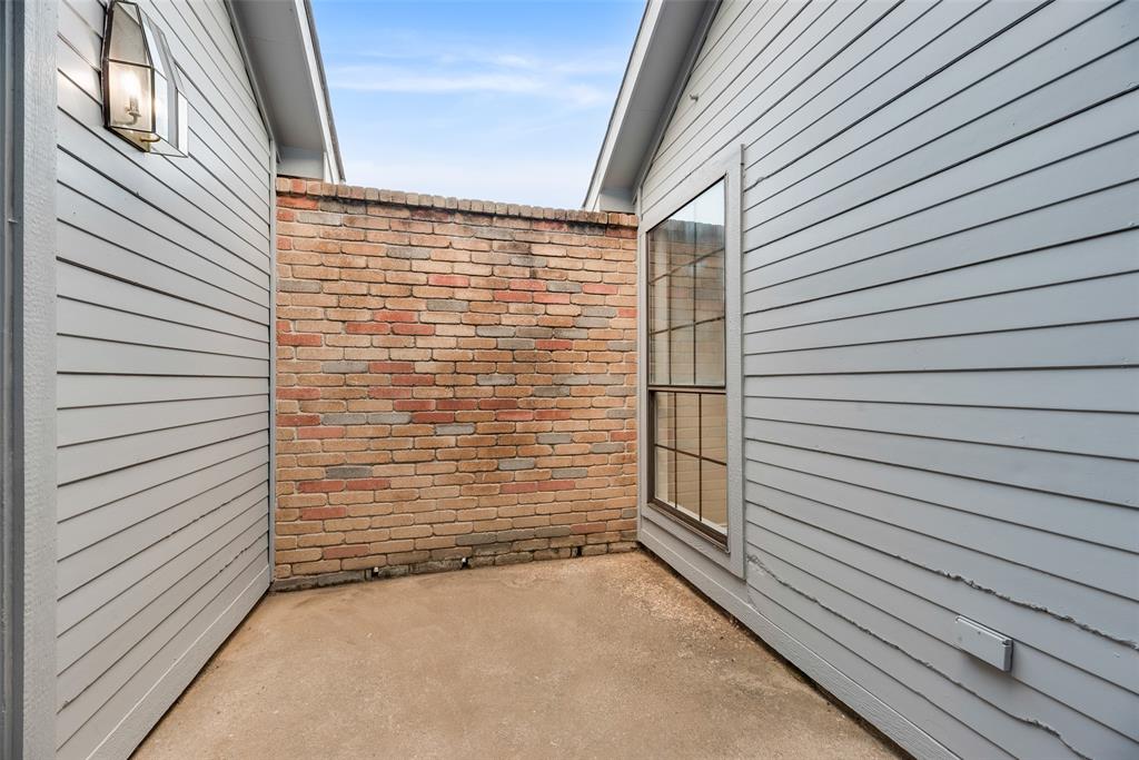 Paved courtyard featuring a brick privacy wall, exterior wall lantern, and a multi-pane window