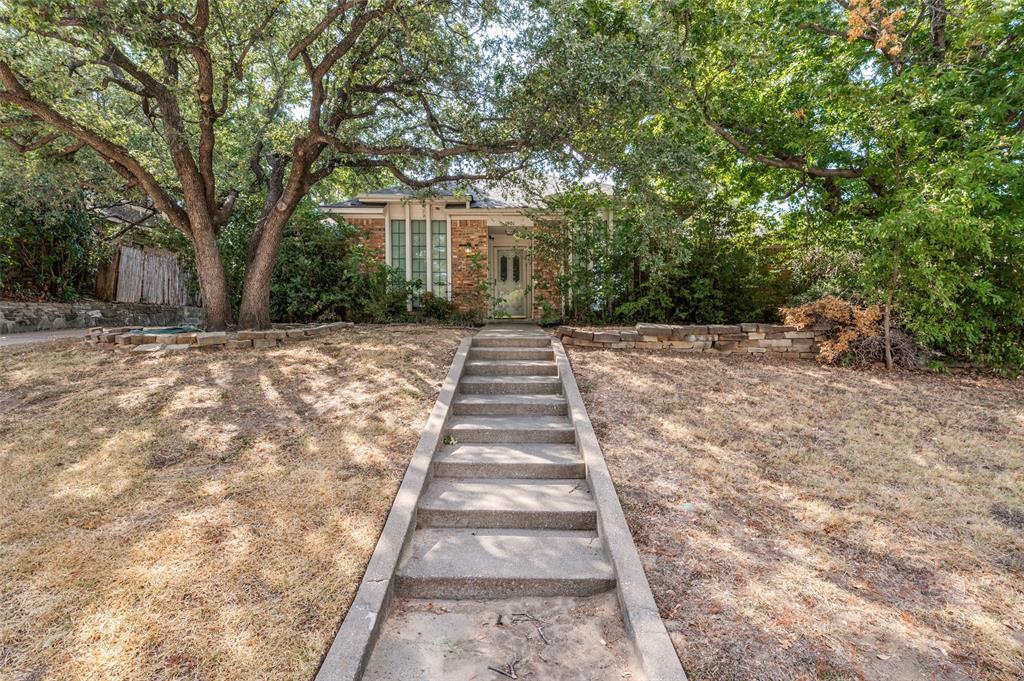 Brick facade residence with a concrete walkway, mature trees, and a stone retaining wall Brick facade residence with a concrete walkway, mature trees, and a stone retaining wall