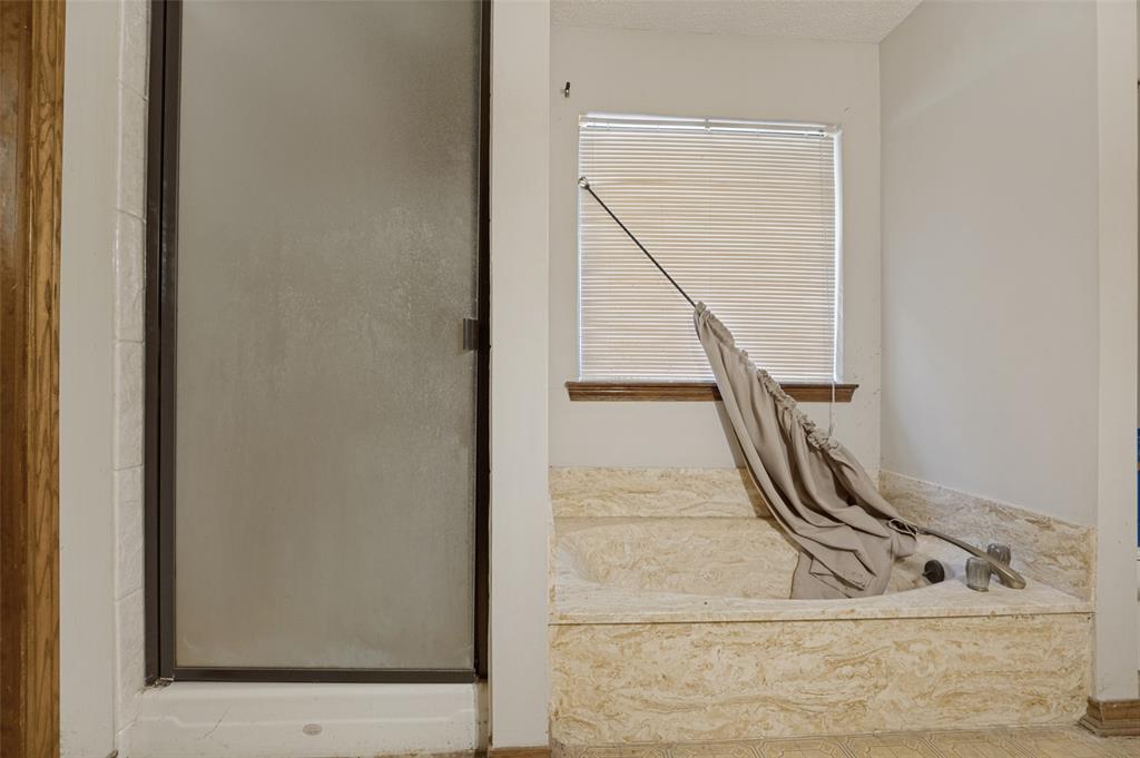 Built-in soaking tub with stone surround, a window with horizontal blinds, and a glass-enclosed shower