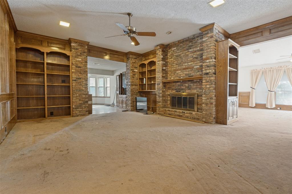 Brick-clad fireplace with metal grate, built-in wooden shelving, wooden paneling, and a ceiling fan with integrated lighting