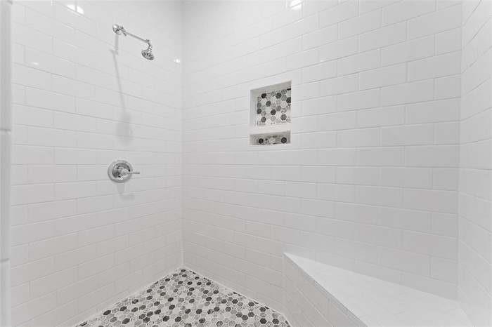 Walk-in shower with white subway tile, mosaic tile flooring, shower niche, built-in bench, and polished chrome fixtures