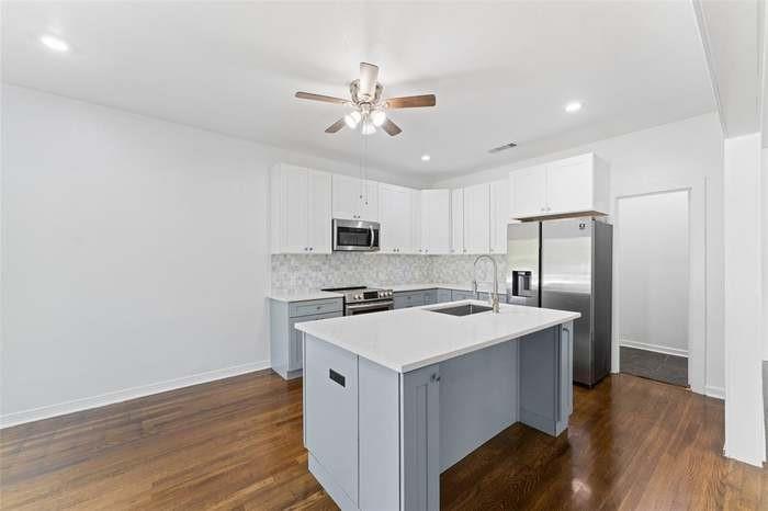Modern kitchen featuring a central island with a sink, white countertop, and gray cabinetry Modern kitchen featuring a central island with a sink, white countertop, and gray cabinetry