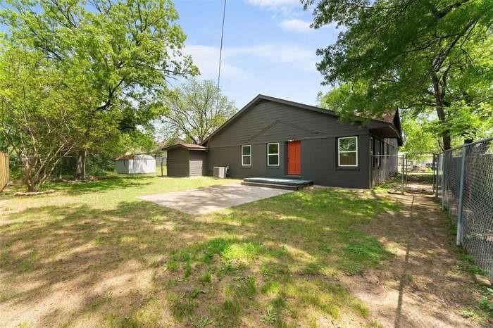 Rear exterior with a concrete patio, dark gray siding, an orange entry door, and white window frames