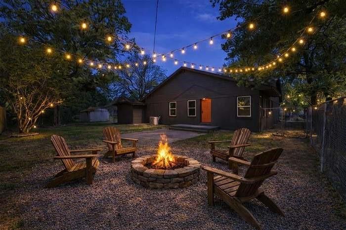Spacious backyard featuring a stone-clad fire pit, gravel ground cover, and a string light installation