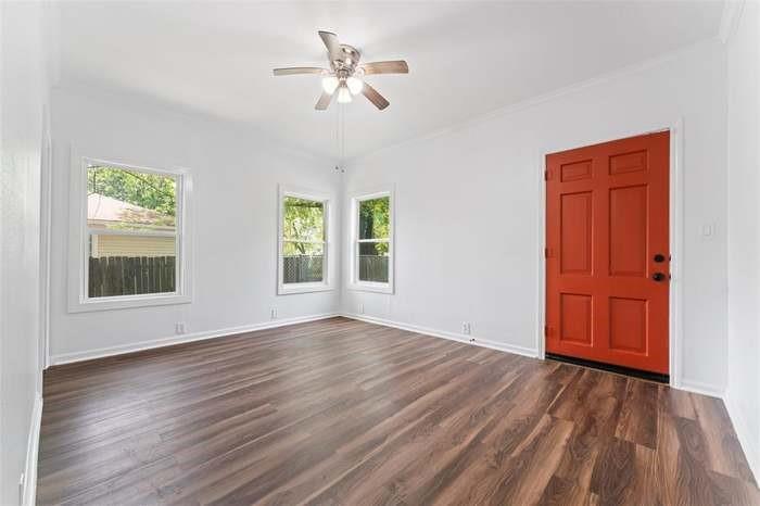 Vibrant paneled entry door, wood-finish flooring, multiple windows, classic white trim, and a ceiling fan with integrated lighting