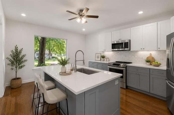 Kitchen featuring wood-finish flooring, a central island with an undermount sink, stainless steel appliances, two-tone cabinetry, and recessed lighting Kitchen featuring wood-finish flooring, a central island with an undermount sink, stainless steel appliances, two-tone cabinetry, and recessed lighting