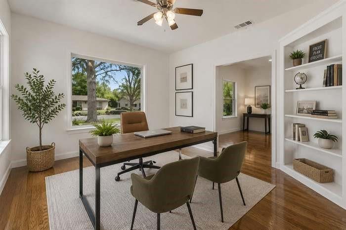 Hardwood flooring, recessed built-in shelving, a ceiling fan, and large windows create a bright interior