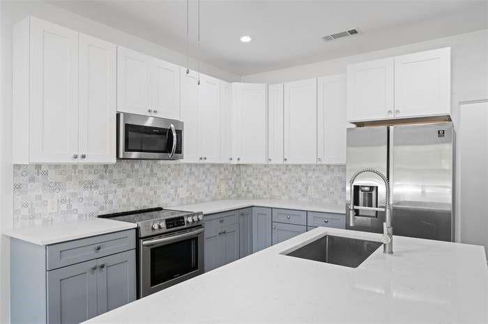 Kitchen featuring two-tone cabinetry, stainless steel appliances, patterned tile backsplash, white countertops, and an undermount sink with a pull-down faucet Kitchen featuring two-tone cabinetry, stainless steel appliances, patterned tile backsplash, white countertops, and an undermount sink with a pull-down faucet