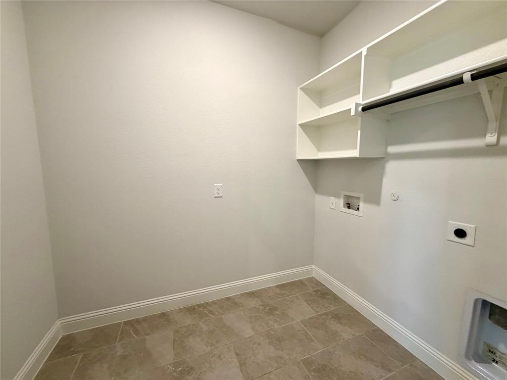 This spacious and highly functional laundry room features durable, easy-to-clean tiled flooring throughout the entire space. It comes fully equipped with convenient built-in shelving units for maximum storage, a sturdy integrated hanging rod for air-drying garments, and significant extra square footage that provides enough room to accommodate an additional refrigerator or freezer.