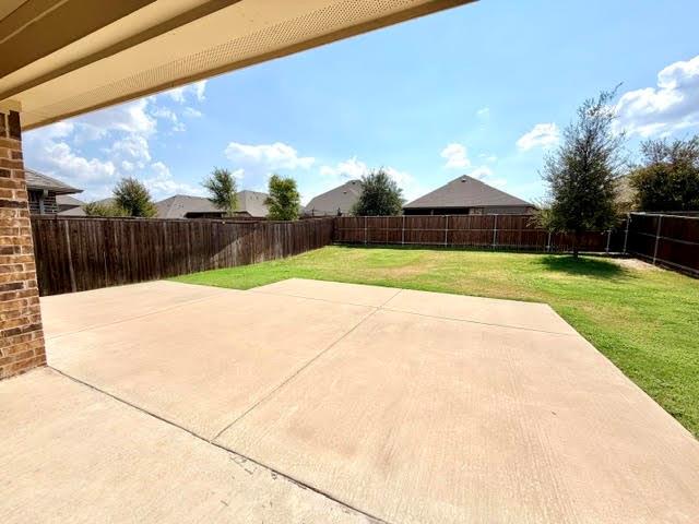 Covered patio with a concrete surface, brick wall, and expansive lawn surrounded by a privacy fence