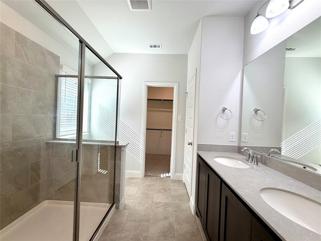 This primary bathroom features a spacious, modern walk-in shower finished with a clean clear glass enclosure and elegant, durable tile surround, perfectly complemented by a functional and stylish dual-sink vanity arrangement.
