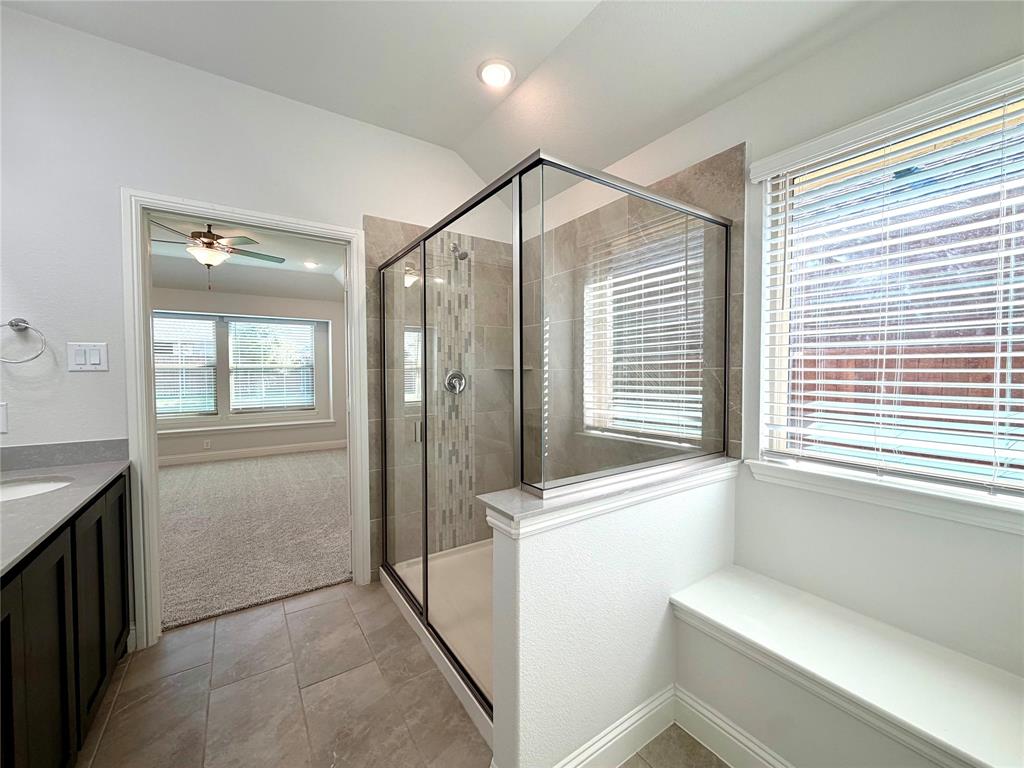 This stunning primary bathroom features a spacious walk-in shower enhanced by a sleek glass enclosure, exquisite custom tile work, and a convenient, beautifully integrated built-in bench for added comfort and functionality.