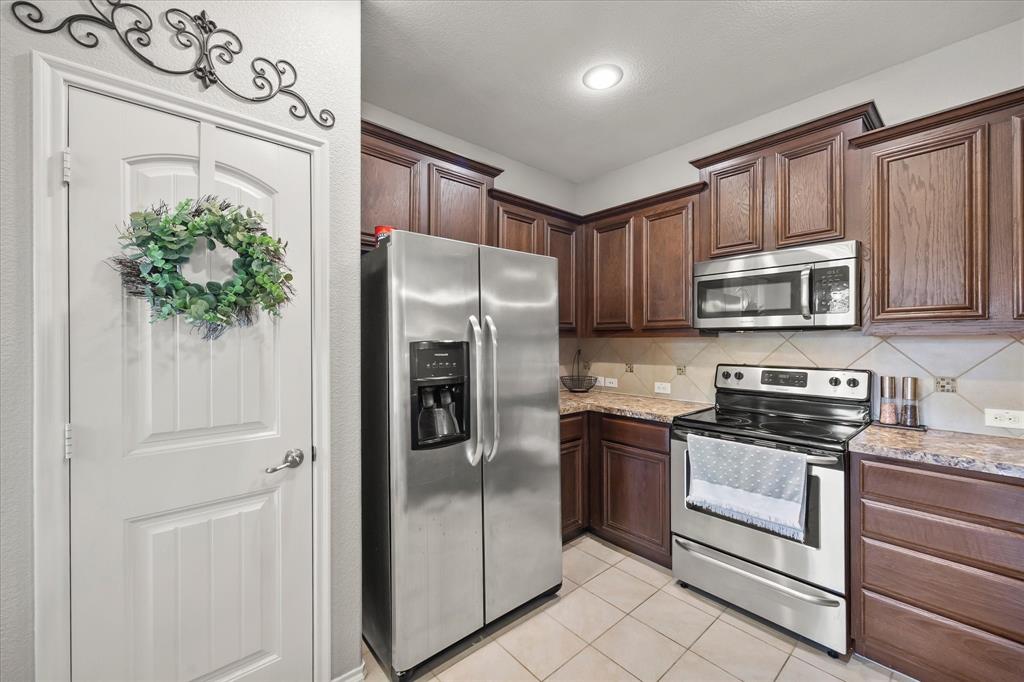 Kitchen featuring wood cabinetry, stainless steel appliances, tile flooring, and a tile backsplash