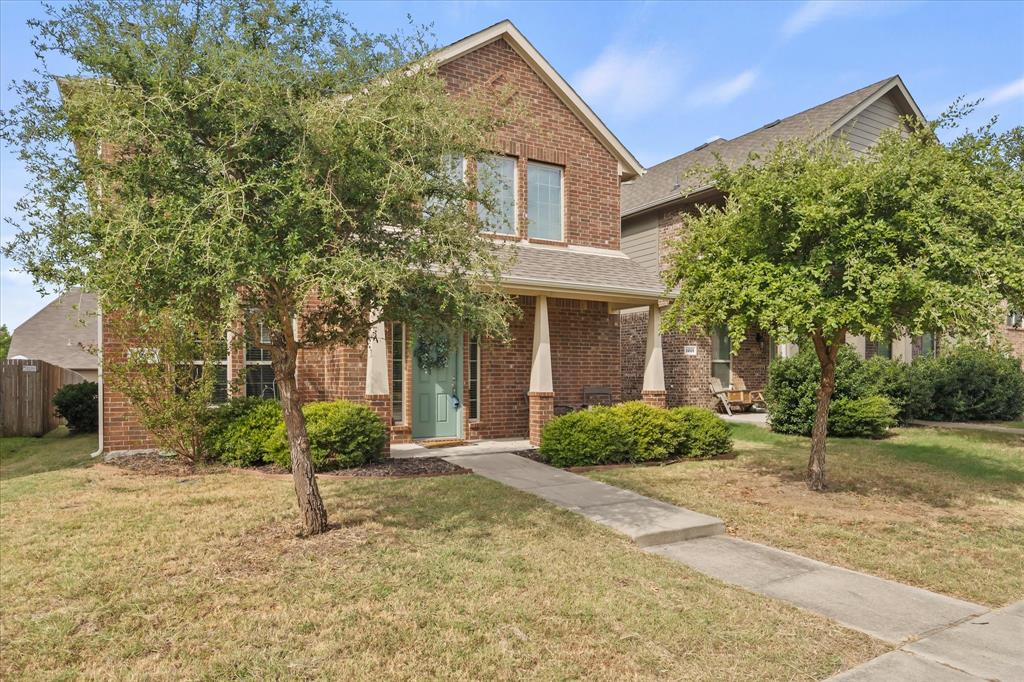 Brick exterior facade with a covered entry, established landscaping, a concrete walkway, and a partial privacy fence