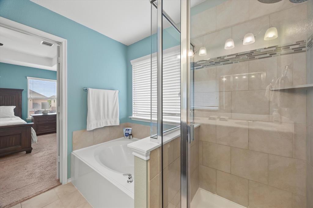 Built-in soaking tub, glass-enclosed shower with tiled walls, decorative tile shower accent, and a row of four vanity lights