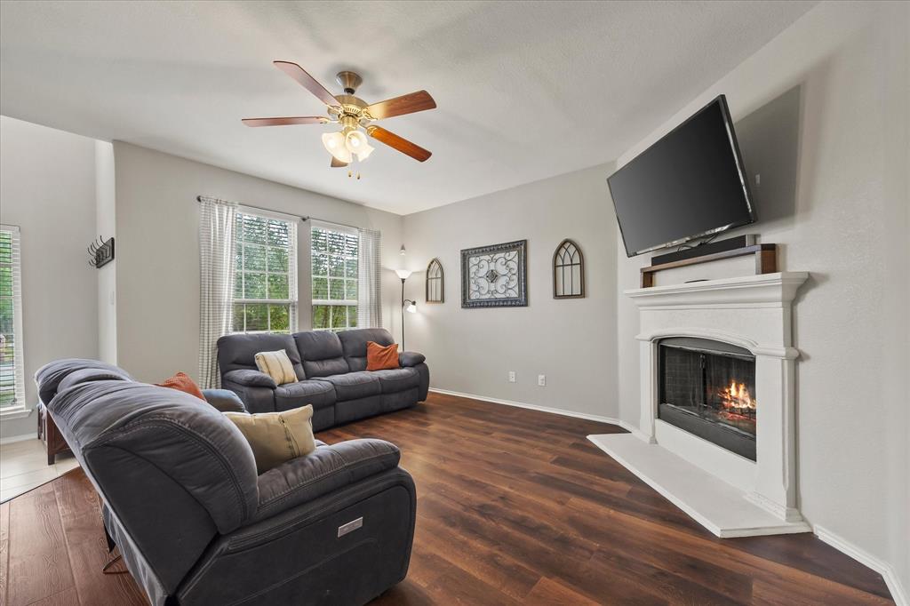Living area featuring wood-finish flooring, a white mantel fireplace, and multiple windows