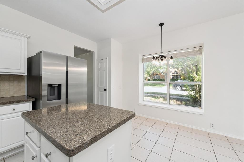 Kitchen featuring an island with stone countertops, white cabinetry, stainless steel refrigerator, tile backsplash, and tile flooring