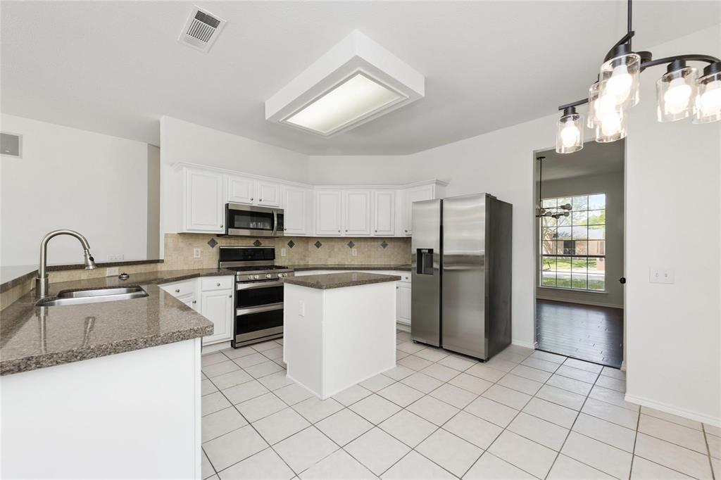 White cabinetry with stainless steel appliances, granite countertops, kitchen island, and tiled flooring