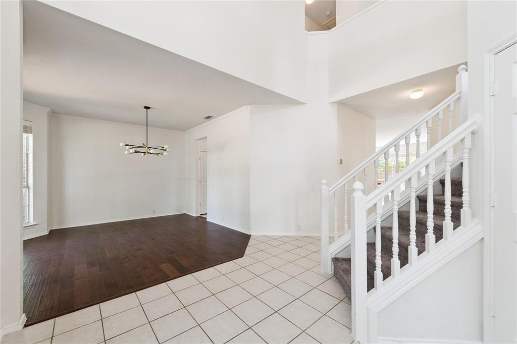 High ceilings featuring an open foyer, wood-finish flooring, a modern chandelier, and a carpeted staircase with white balusters