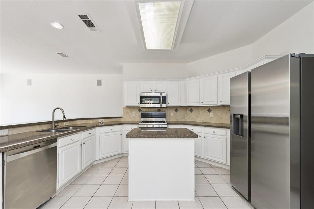 Kitchen featuring white cabinetry, stainless steel appliances, a center island, stone-finish countertops, and a tiled backsplash