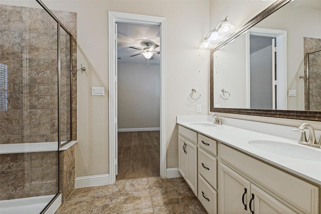 Dual vanity, decorative framed mirror, attached wall sconce lighting, and a walk-in shower with tiled walls and a glass enclosure