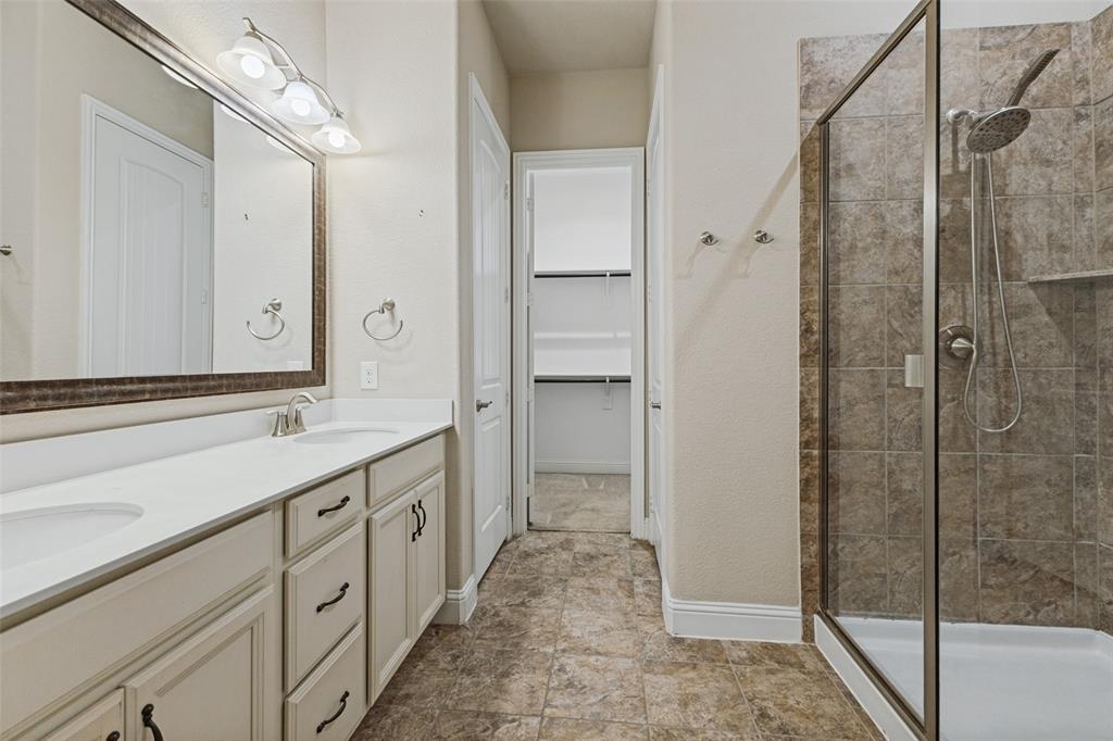 Vanity with dual sinks, framed mirror,  decorative light fixture, large walk-in shower
