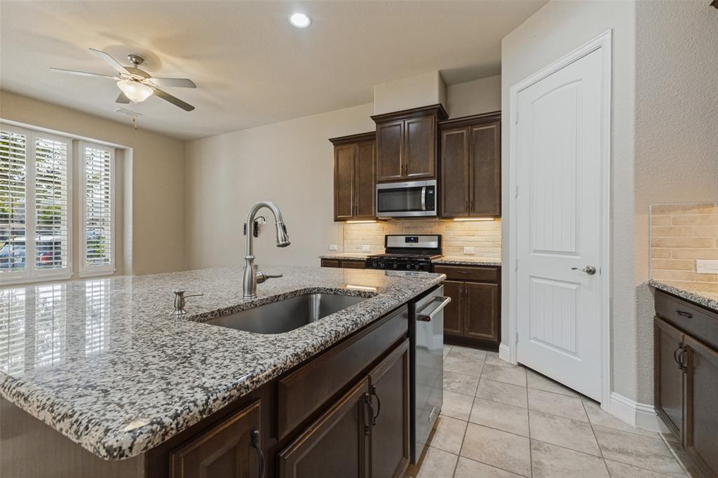 Kitchen island with granite countertop and undermount sink, stainless steel appliances with gas cooktop range, and walk-in pantry