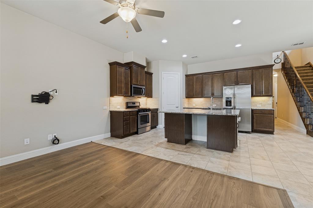 Open-concept layout featuring wood-flooring, a kitchen island with granite countertop, stainless steel appliances, and dark wood cabinetry