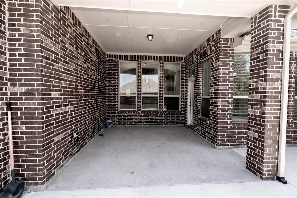Covered concrete patio featuring dark brick walls, multiple windows, a white door, and a recessed ceiling light