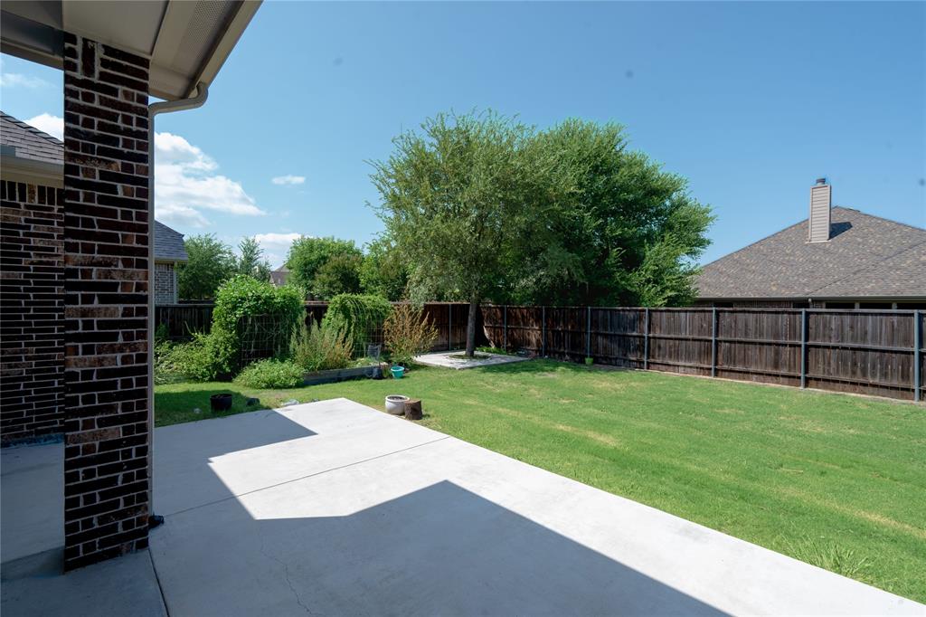 Expansive concrete patio with a brick support column, a wood privacy fence, and a manicured lawn