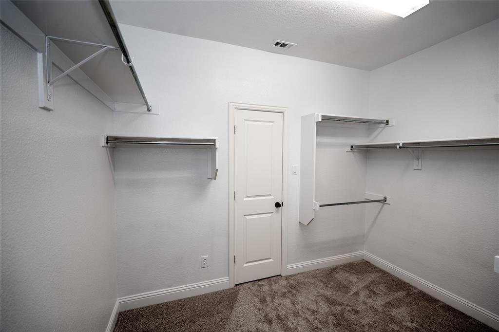 Wall-mounted shelving with integrated hanging rods, carpeted flooring, white trim, and overhead lighting