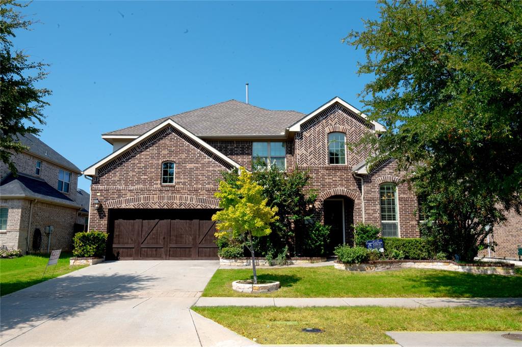 Multi-tone brick facade with a gabled roofline, arched entry, and integrated two-car garage featuring wood-finish doors